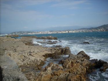 A la pointe rocheuse de l'&icirc;le battue par les flots, on aper&ccedil;oit la ville de Cannes